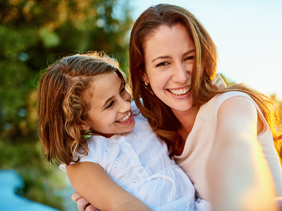 Smiling mother and daughter hugging outdoors and taking a selfie together on a sunny day